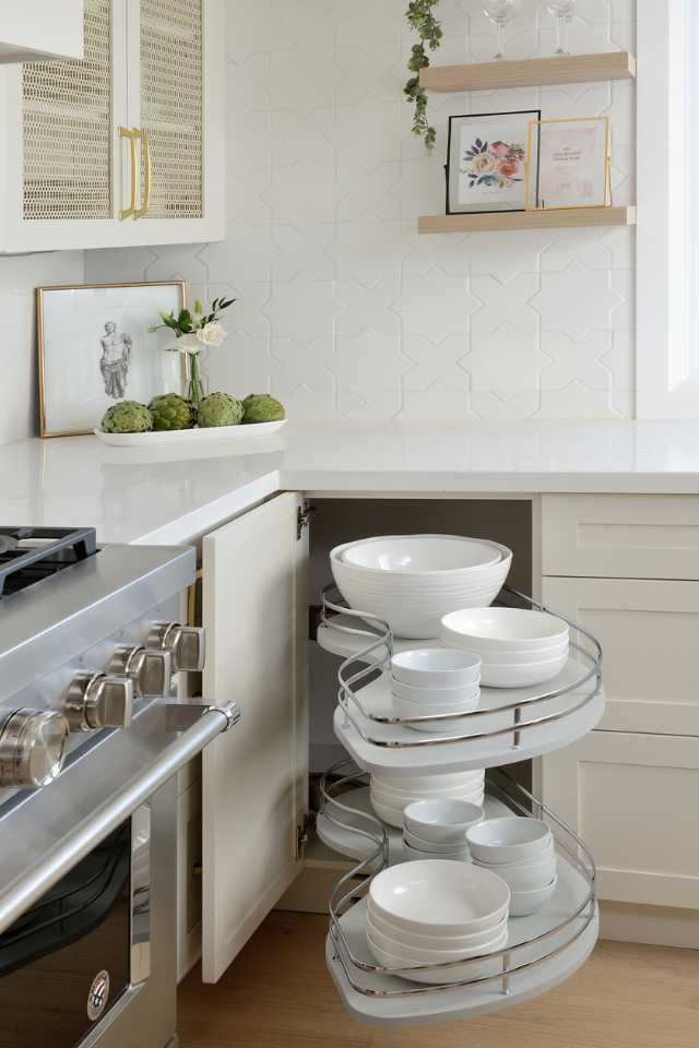 custom built hidden shelving for dishware in white designer kitchen with gold accents